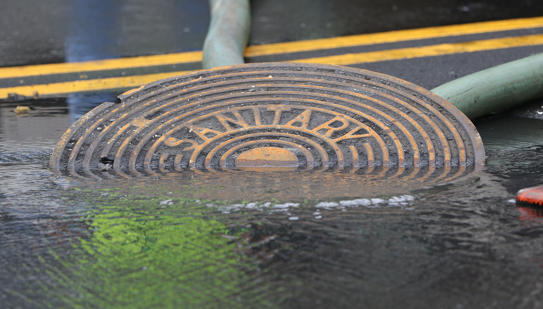 Workers flush a manhole cover along Atkinson Drive after 500,000 gallons of sewage leaked out closing Waikiki Beach. 24 aug 2015. photograph by Cory Lum/Civil Beat