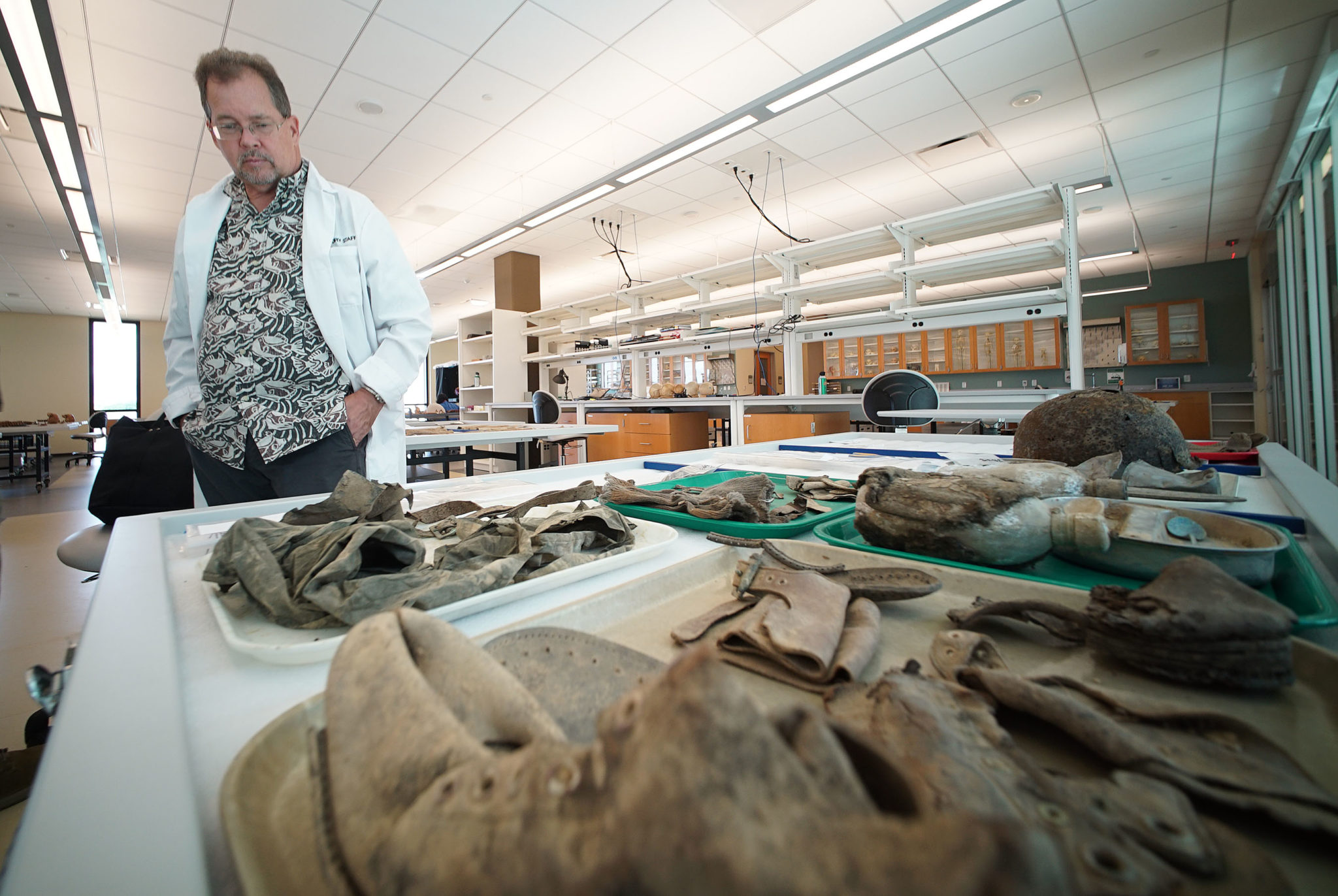 Defense POW MIA Accounting Agency Dr William Belcher with foreground right, boots, helmets, gloves and military equipment that was with the remains returned from North Korea.