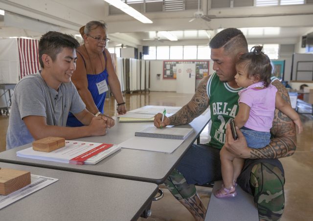 Voter precinct volunteers Tyler Maruno, left, and Letitia Corpuz, center, help Matt Coleman, right, holding his daughter Natalee, sign-in before voting at Lanakila Elementary School, Saturday, Aug. 11, 2018, in Honolulu.