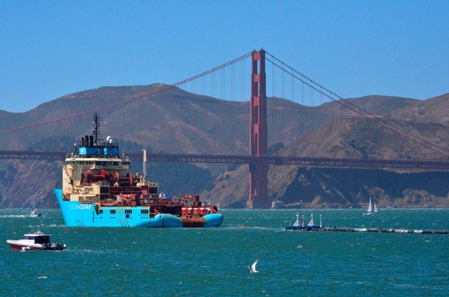 File - In this Sept. 8, 2018 file photo, a ship tows The Ocean Cleanup's first buoyant trash-collecting device toward the Golden Gate Bridge in San Francisco en route to the Pacific Ocean. The trash collection device deployed to corral plastic litter floating between California and Hawaii in an attempt to clean up the world's largest garbage patch is not collecting any trash. But Boyan Slat, who launched the Pacific Ocean cleanup project, told The Associated Press in an interview Monday, Dec. 17, 2018, he is confident the 2,000-foot (600-meter) long floating boom will be fixed. (AP Photo/Lorin Eleni Gill, File)
