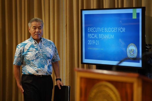 Governor David Ige walks into press conference past computer screen at the Capitol.