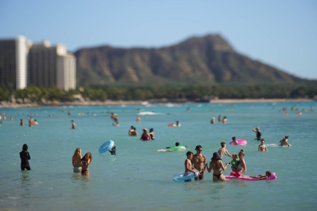 Visitors frolic at Waikiki Beach with Diamond Head as a backdrop.