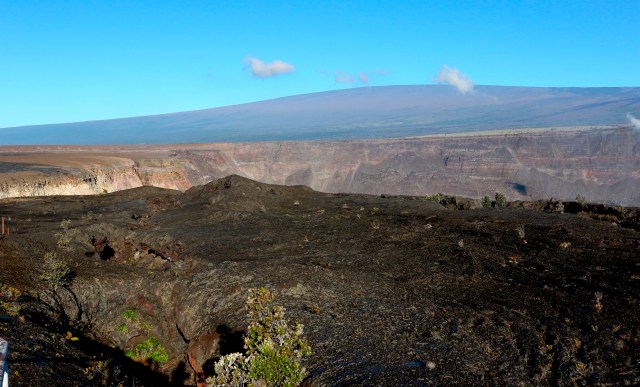 In this April 25, 2019 photo, Hawaii's Mauna Loa volcano, background, towers over the summit crater of Kilauea volcano in Hawaii Volcanoes National Park on the Big Island. Federal officials raised the alert level for Mauna Loa, the world's largest active volcano, Tuesday, July 2, 2019. The U.S. Geological Survey changed the level from normal to advisory after observing a slight increase in earthquakes and ground swelling over the past several months. Officials say the increased alert level does not mean an eruption is imminent. (AP Photo/Caleb Jones)