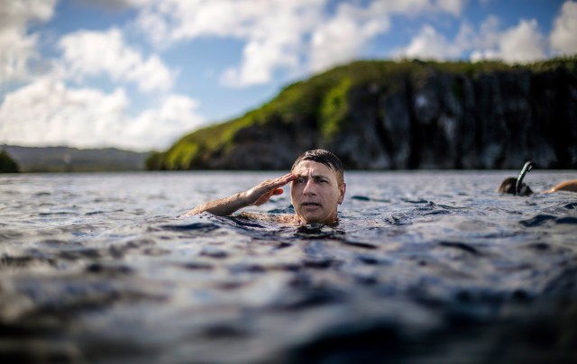 Walter Denton Guam Sex Abuse a former Army sergeant, treads water while saluting a U.S. flag on a nearby cliff of a military base during the morning broadcast of the national anthem as he swims with his brother in Agat, Guam, Saturday, May 11, 2019. "It helped me to stay focus every single day," Denton says of his time in the military and coping with a sexual abuse by a priest over 40 years ago, allegations detailed in a lawsuit. "Every morning I looked forward to putting on my uniform and going to work. It was a distraction." Former Archbishop of Agana, Anthony Apuron denies the allegations. (AP Photo/David Goldman)