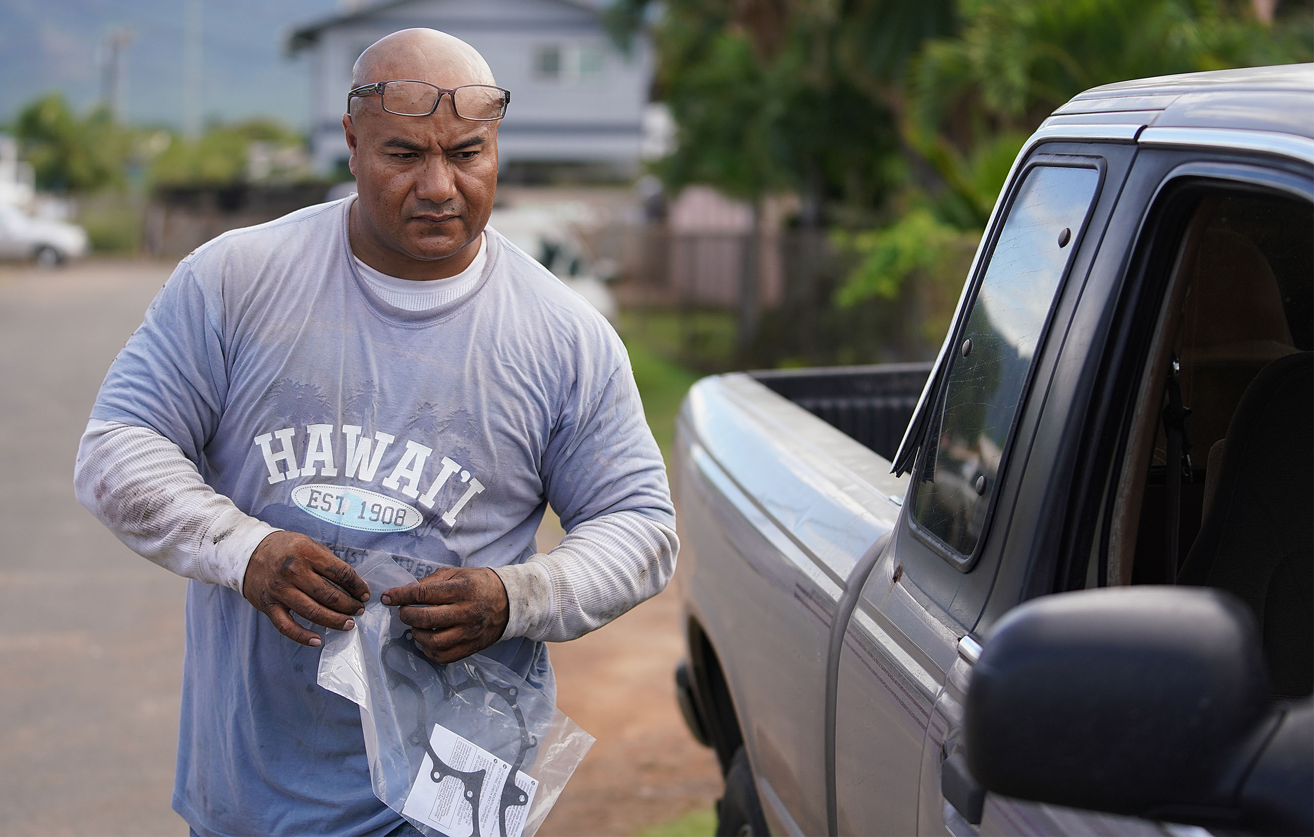 Sefo Fataai fixing truck out in Maili Waianae. Sefo holds water pump parts for a truck he is fixing outside along the road.