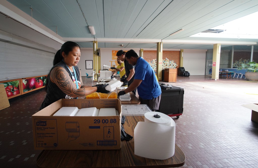 Lizz ( no last name) puts hamburger steak lunches into box to be brought outside for curbside pickup by parents/kids.