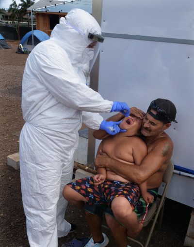 A volunteer from the the COVID Command Mobile Unit, of the Premier Medical Group Hawaii, performs a swab test on Hui Mahi'ai Aina resident, Luke Mossman 7yrs. old while his dad, Dylan Spencer, holds him still on his lap, Sunday, April 26, 2020. (Ronen Zilberman photo Civil Beat)