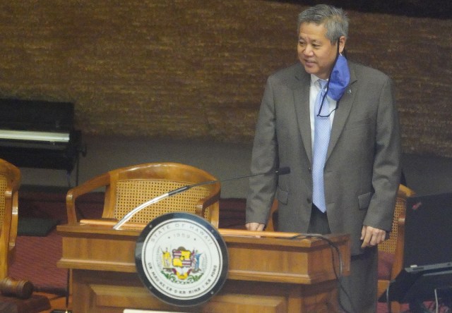 House Speaker Scott Saiki stands at podium with mask dangling on his ear before session begins during COVID-19 pandemic. June 22, 2020