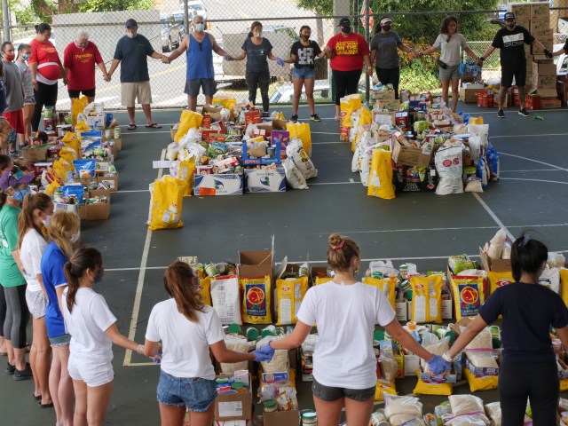 Oahu based canoe club volunteers and community members circle up and hold hands in prayer as they prepare to hand out food donations to families in the Papakolea Hawaiian Homestead neighborhood of Honolulu, HI, Sunday, June 14, 2020. Several local canoe clubs came together to organize this food drive and distribution event during what would normally be their busiest time of competitions, all canceled due to COVID-19 restrictions. (Ronen Zilberman photo Civil Beat)