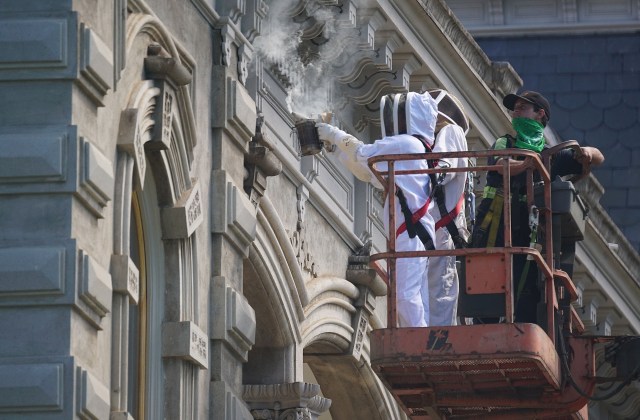 Left, Jasmine Joy from Beelieve uses smoking coconut husk with colleague Elko Evans and right, Bob’s Equipment Sales and Rentals lift operator Paul Pestana to survey the bee nest on the Iolani Palace roof eaves. Later, Elko will use a Sawzall to cut into and remove the bee colony.