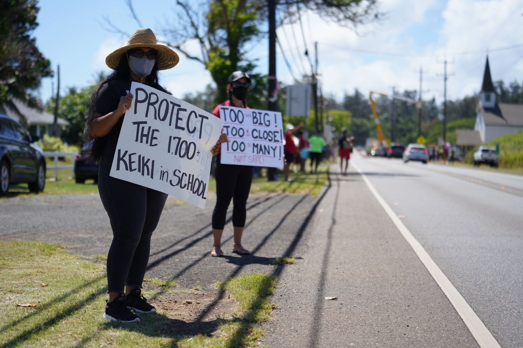 Laie resident, Sonnie Muaina and right, Oriana McCallum from Kahuku hold signs along Kamehameha Highway in Kahuku against the windmills.