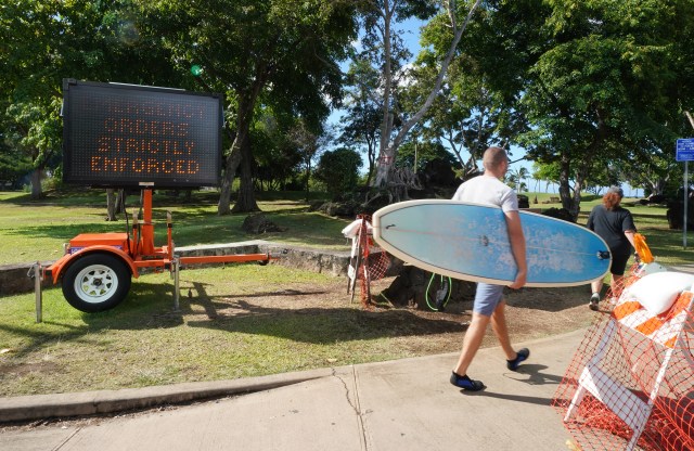 Beachgoer walks past Ala Moana Beach park sign ‘Emergency Orders Strictly Enforced’. Today, Mayor Caldwell announced another 2 weeks of stay at home with opening beaches and parks with restrictions. September 8, 2020