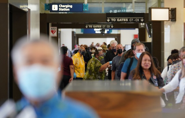 Hundreds of passengers arrive and wait in a line with Governor Ige in foreground during press conference. Arriving passengers are screened if they have pre-travel testing required to avoid the 14-day traveler quarantine. Tests are only accepted from trusted testing and travel partners. October 15, 2020