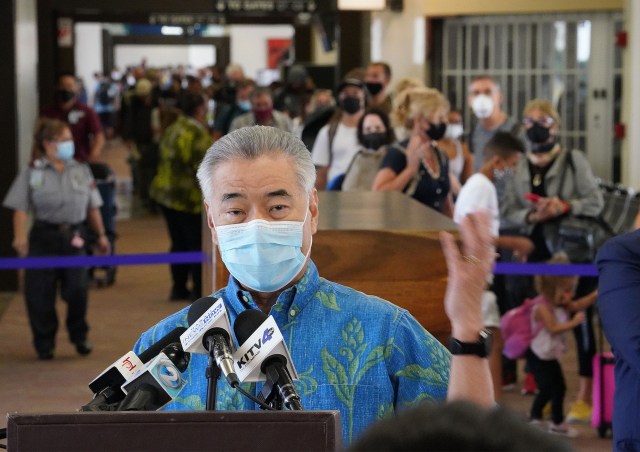 Hundreds of passengers arrive and wait in a slow moving line with Governor Ige in foreground during press conference. Arriving passengers are screened if they have pre-travel testing required to avoid the 14-day traveler quarantine. Tests are only accepted from trusted testing and travel partners. October 15, 2020