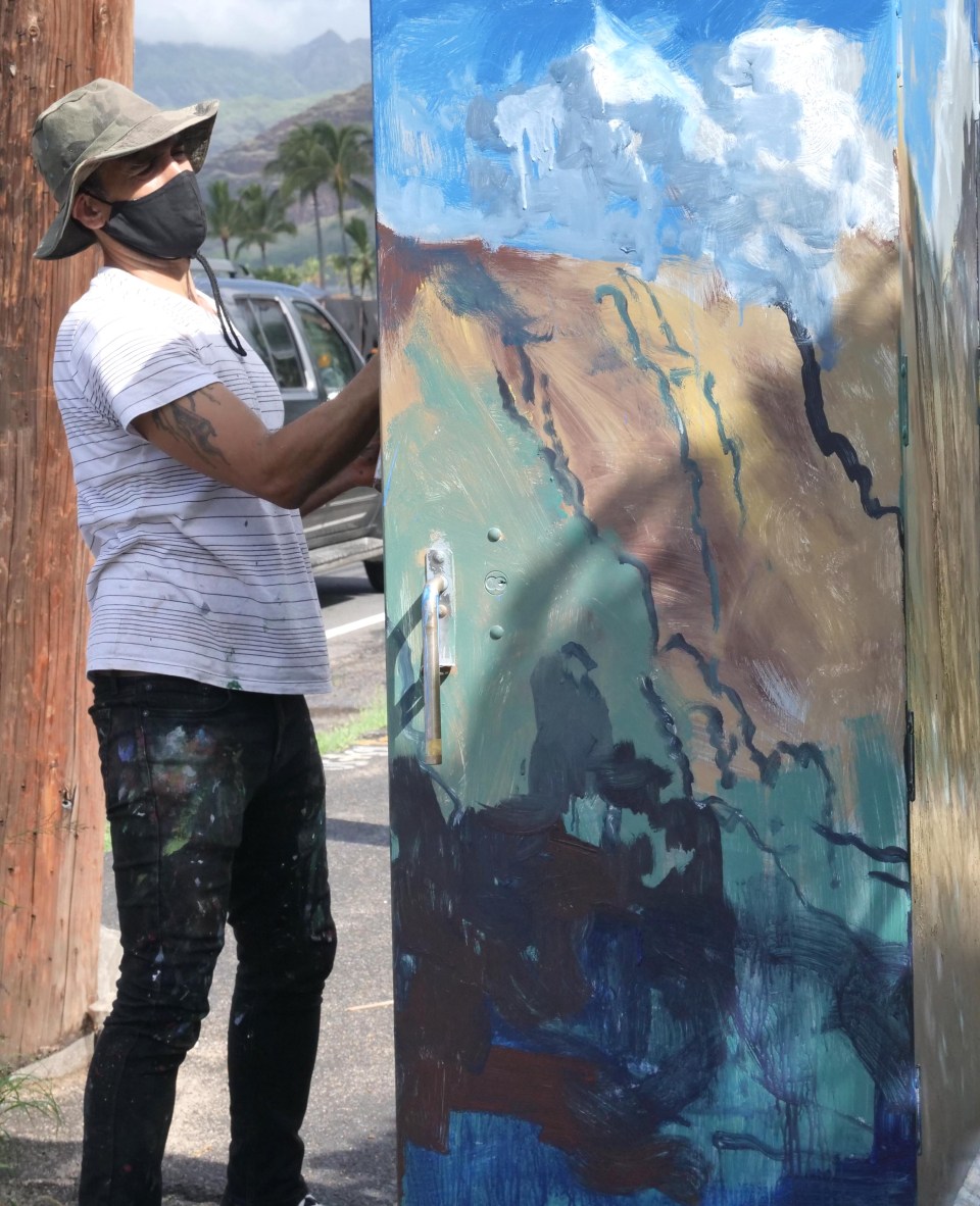 Waianae resident and artist Solomon Enos paints the surrounding mountains onto a traffic box on the Farrington Hwy in Waianae, HI, Saturday, October 24, 2020. The piece is part of a community project coordinated by Valley of Rainbows to beautify the 11.5-mile stretch of Farrington Highway in Leeward Oahu .  Artists will paint up to 25 traffic boxes with murals showcasing the beauty, legends, nature and stories of the Waianae Coast. 