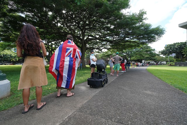 Waimanalo resident Mark Hartsock wears a Hawaiian flag while standing in a long line to vote in the 2020 General Election near Honolulu Hale.