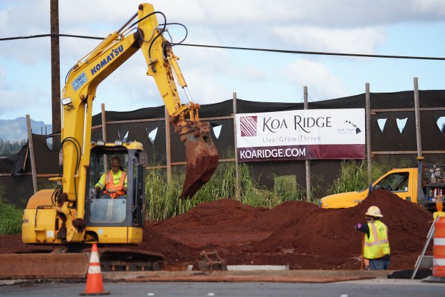 Workers on Ka Uka Boulevard with Koa Ridge development banner in background.