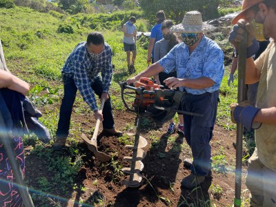 George Kahumoku uses a power tool to dig a hole while another volunteer assists with a pickax.