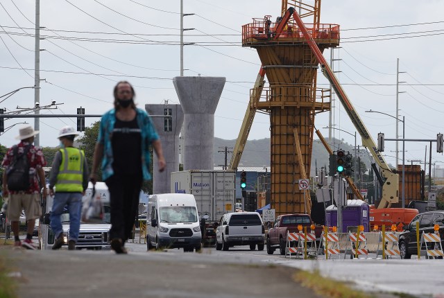Pedestrians walk along Dillingham Boulevard with rail guideway supports being built towards metropolitan Honolulu.