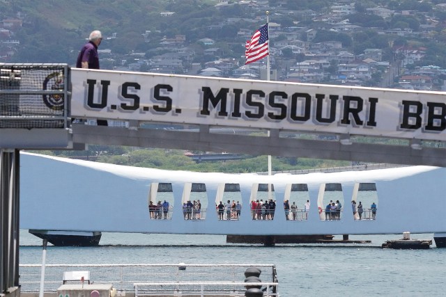 Person walks up ramp to visit the USS Missouri with the USS Arizona Memorial in the background at Joint Base Pearl Harbor-Hickam.
