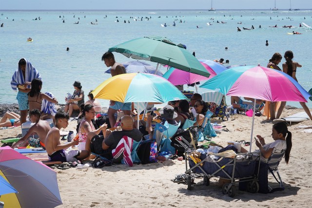 People gather under umbrellas near Kuhio Beach during COVID-19 pandemic.
