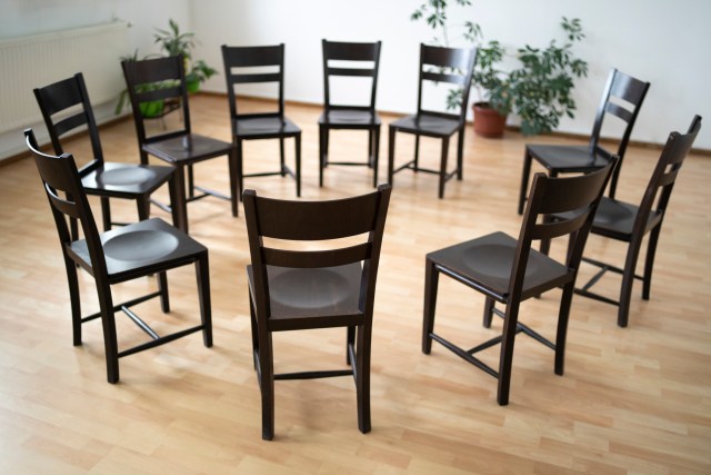 A circle of empty chairs in a plain room with a wooden floor