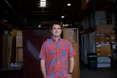 Founder of Reuse Hawaii, Quinn Vittum, stands in front of their warehouse filled with appliances, furniture, Christmas decoration and more.