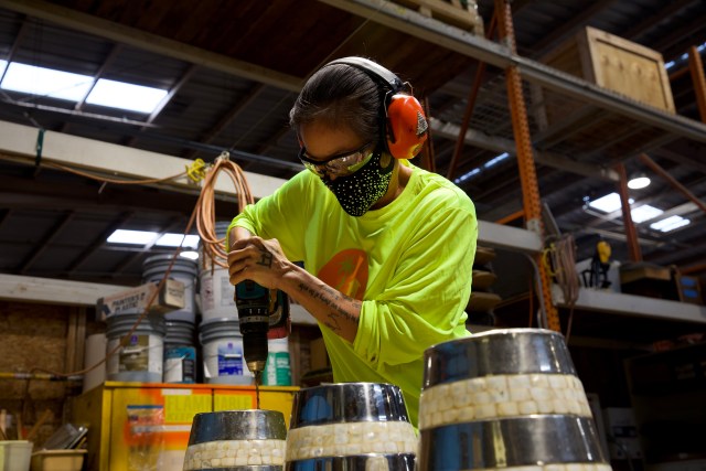 Keala Fung, Kupu Aina Corps. alumni, presses down on the drill to turn former buckets into plant pots.