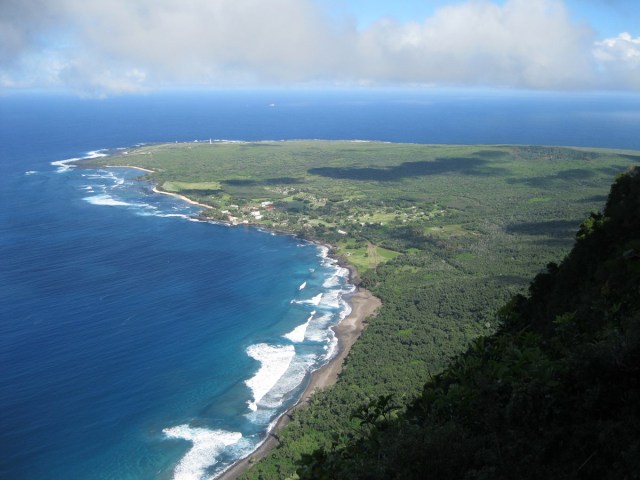 An aerial view of an green peninsula jutting out into the water below tall sea cliffs