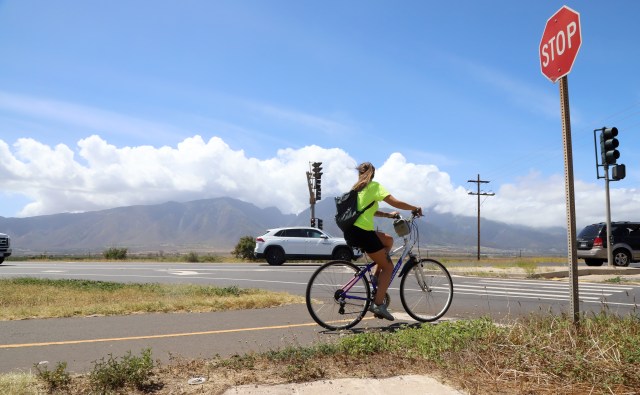A photograph of Liz Woodall riding her bike through a Maui intersection.