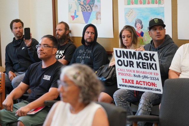 People in opposition to the Department of Education's mask mandate hold a sign at the DOE board meeting.