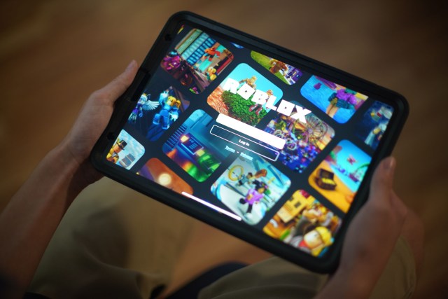 A child holds an ipad with Roblox game prompt.