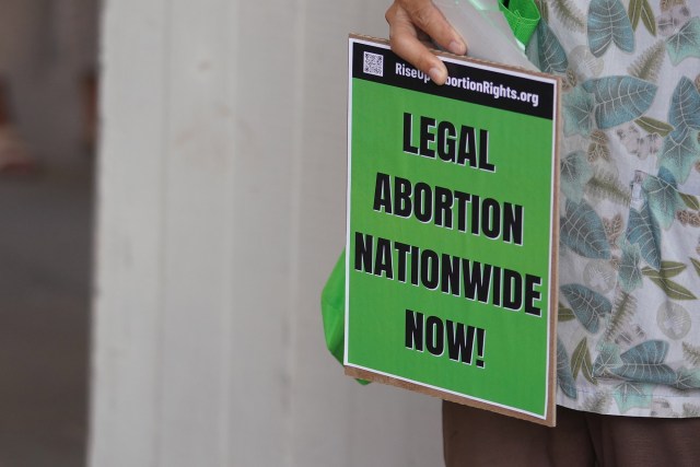 A person holds a 'legal abortion nationwide now' sign at a press conference called by the Hawaii Abortion Collective to announce The Official Hawaii Abortion Guide at the Capitol Rotunda.