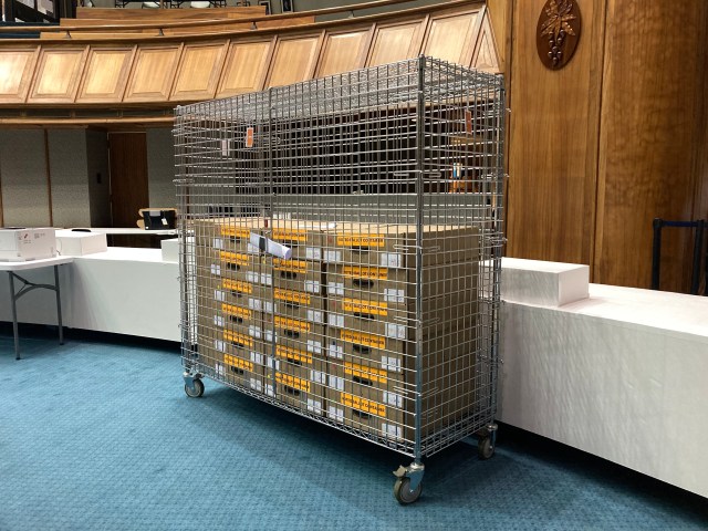 A cage of labeled cardboard boxes containing ballots sits in the State Senate Chamber.