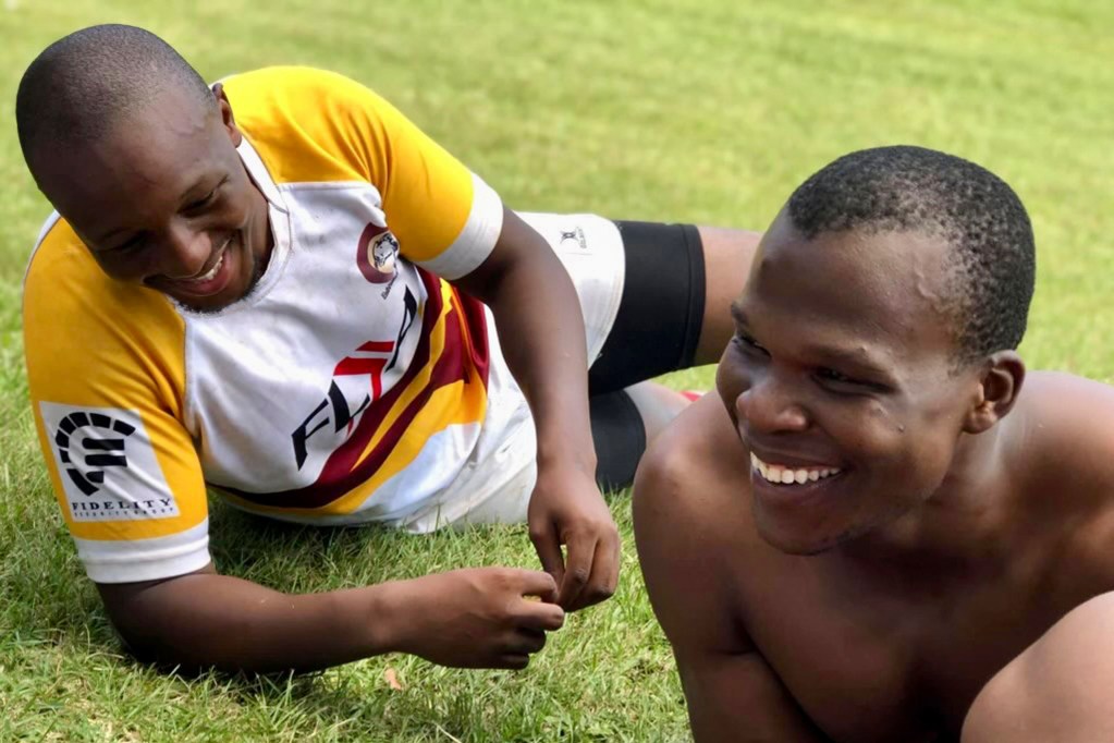 In this undated photo provided by Lindsay Myeni, is Lindani Myeni, foreground with no shirt on, resting on the grass after a rugby match in Eshowe, South Africa. Myeni was fatally shot by Honolulu police in 2021 after he physically attacked officers, who responded when an upset occupant of a home complained a stranger had entered uninvited wearing a feathered headband and made bizarre comments. Results of studies of Myeni's brain tissue, obtained by The Associated Press, show the 29-year-old South African rugby player had Stage 3 CTE, or brain trauma caused by repeated concussions. (Lindsay Myeni via AP)