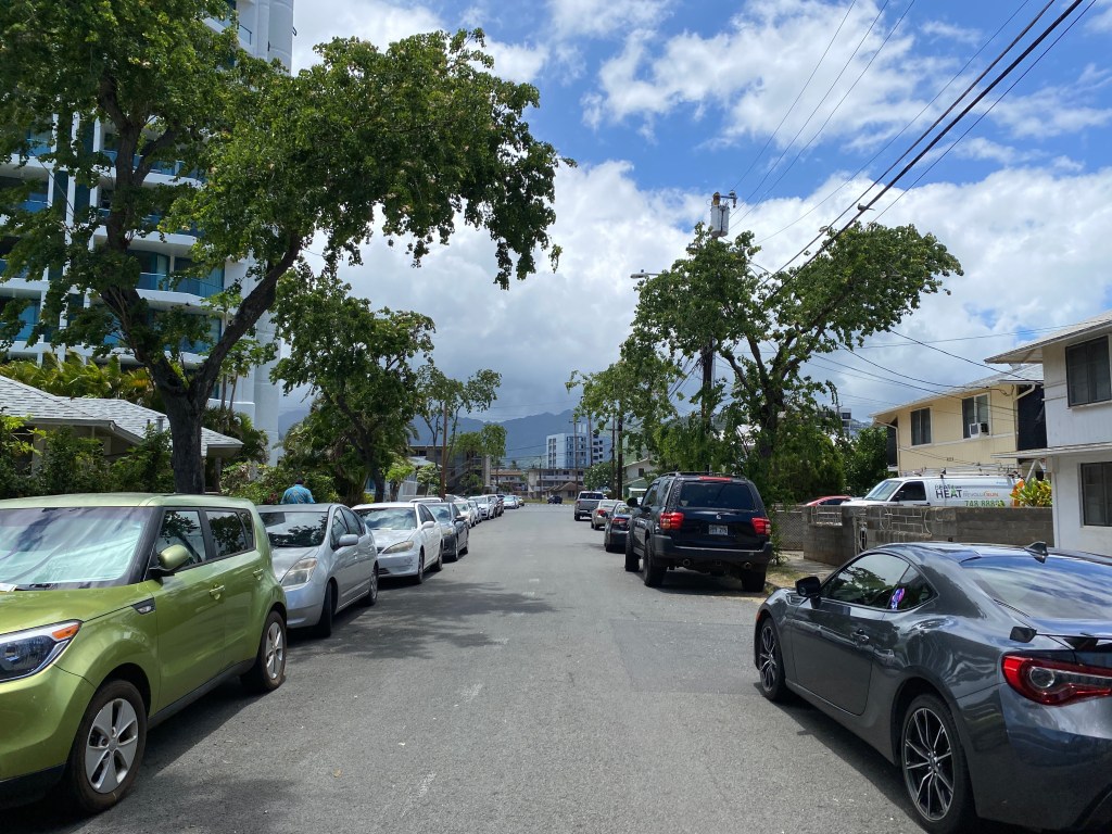 Cars line both sides of a narrow street