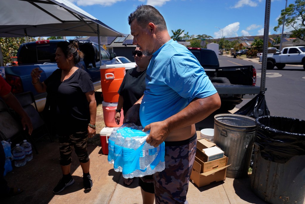 Keshia Santos, from left, and Charles Kahunanai deliver water Sunday, Aug. 13, 2023, in Wahikuli neighborhood, north of Lahaina town and south of Kaanapali. Charles lost his home in the fire. fA large fire consumed areas of West Maui last week. Utilities have not been fully restored. (Kevin Fujii/Civil Beat/2023)
