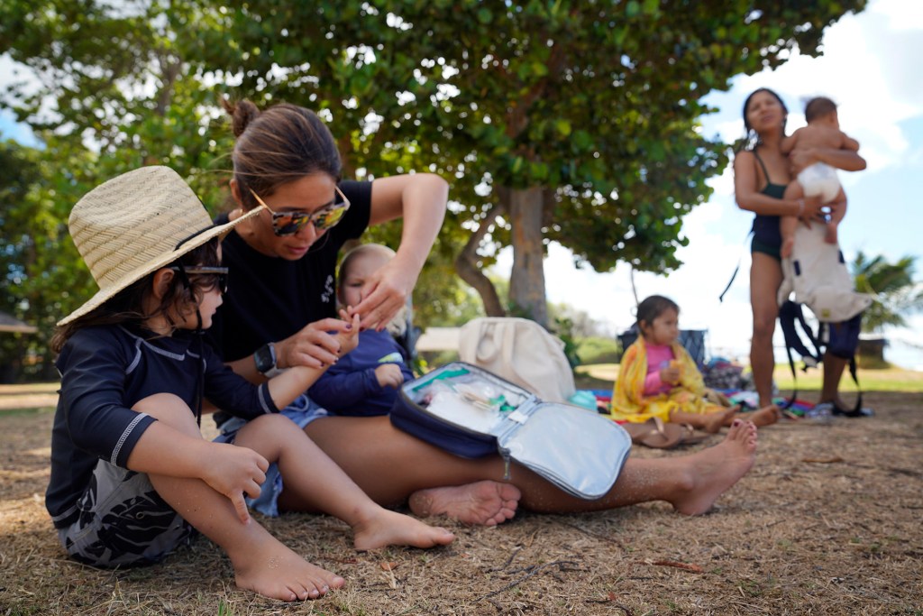 Ekuale Taua’a has Surfing Mom’s Sachiko Stokes look at something poking his finger during the Ewa group’s weekly outing Tuesday, Aug. 15, 2023, at White Plains Beach in Ewa Beach. The moms take turn surfing while other moms watch the keiki. (Kevin Fujii/Civil Beat/2023)