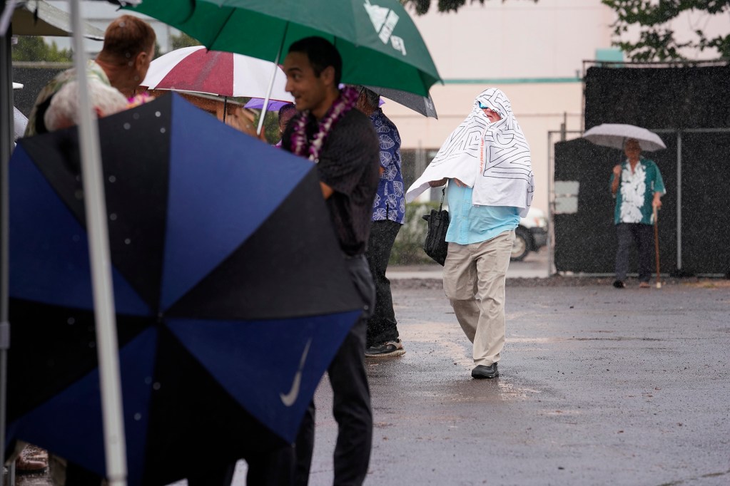 Attendants seek cover as rain falls heavily before the Wahiawa Civic Center’s ceremonial ground breaking Tuesday, Sept. 26, 2023, in Wahiawa. The towel-wearing man is none other than Honolulu Civil Beat politics and opinion editor Chad Blair. The almost three-acre site will include two buildings for a courthouse, state offices and City and County of Honolulu satellite city hall. (Kevin Fujii/Civil Beat/2023)