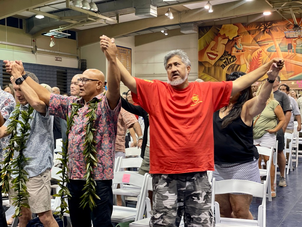 Members of a Lahaina advisory team created by Maui Mayor Richard Bissen raise their arms in a show of unity after a difficult public meeting where officials told residents it could be two years before they could start rebuilding their homes. (Brittany Lyte/Civil Beat/2023)
