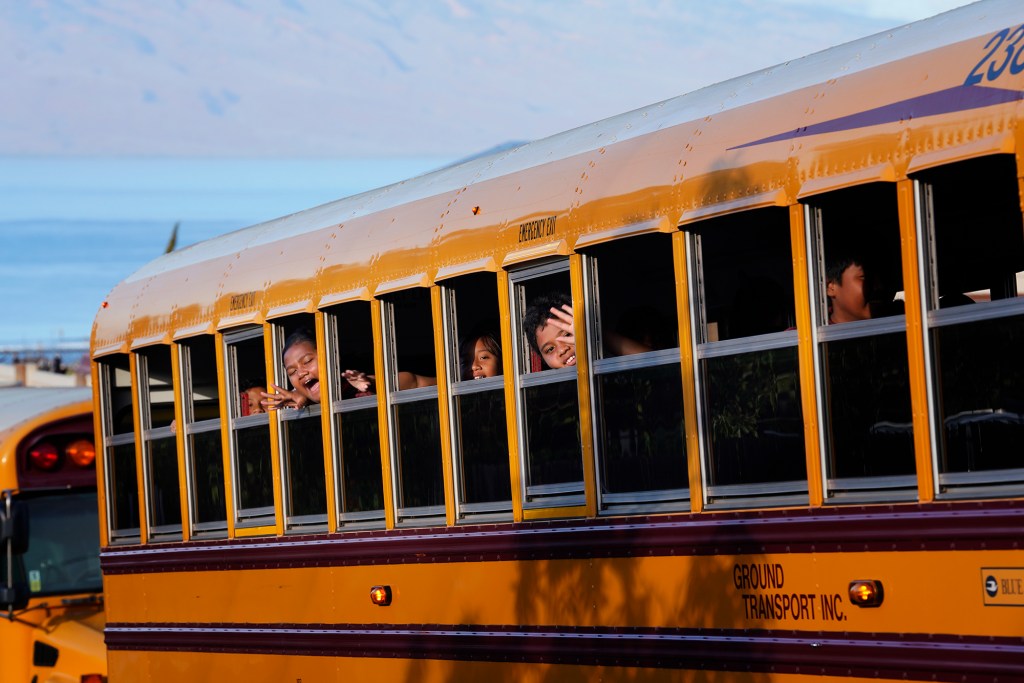 A bus of elementary school students celebrate their return to studying in Lahaina Wednesday, Oct. 18, 2023. Princess Nahienaena Elementary School opened their campus for King Kamehameha III Elementary School to place temporary classrooms. The schools have been closed since the Aug. 8 fire and studying at other schools in Maui. King Kamehameha III Elementary School was destroyed in the blaze. (Kevin Fujii/Civil Beat/2023)
