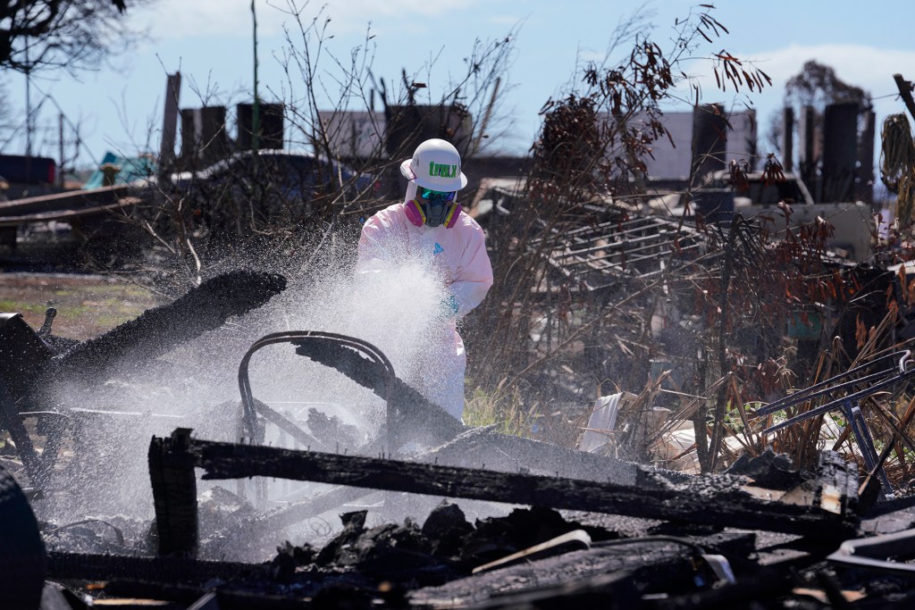 A Truth Excavation employee sprays a soil stabilizer on burned ash and debris Wednesday, Oct. 18, 2023, in Lahaina. Known by its brand name “Soiltac,” once dry, potential hazardous material from burned debris and ash will remain on the ground and not become airborne particles. (Kevin Fujii/Civil Beat/2023)
