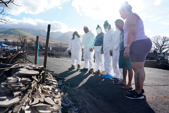 Aziah Fernandez, from left, Anthony Fernandez, Camille Siatris, Bryson Siatris, Devin Siatris, Mario Siatris and U’i Kahue-Cabanting gather to pray before entering their destroyed house Monday, Nov. 13, 2023, in Lahaina. Their home and neighborhood were destroyed in the Aug. 8 fire. (Kevin Fujii/Civil Beat/2023)