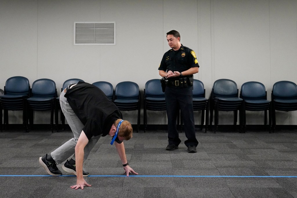KHON photographer Bryce Moore participates in a Honolulu Police Department media workshop on Operating a Vehicle Under the Influence of an Intoxicant also known as OVUII or DUI on Saturday, Nov. 18, 2023, at the HPD training facility in Waipahu. Here Moore wears “Drunk Goggles” which make balance and focus challenging. In this “Walk and Tiurn” test, Moore should be able to walk a certain number of steps, heel to toe, count each step and keep his arms by his side while staying on the blue line. HPD’s message comes as the winter holidays approach. (Kevin Fujii/Civil Beat/2023)