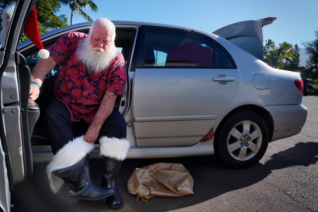Ron Proctor puts on his boots on his Santa Claus boots on Black Friday, Nov. 24, 2023, at the Santa Parade staging area in Kihei. Proctor has played Santa for more than 25 years. He lost his Lahaina home and belongings, including the hand-made Santa suit his daughter made, in the Aug. 8 fire. (Kevin Fujii/Civil Beat/2023)