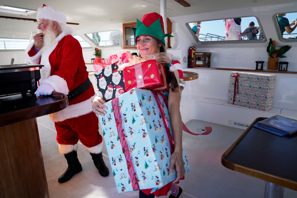 Santa Claus (Ron Proctor) grabs a snack while elf Robin Brown takes the wrapped presents to the deck of the Alii Nui Saturday, Nov. 25, 2023, in Maalaea Bay near Wailuku. The sunset cruise during the holidays becomes the Santa Cruise. (Kevin Fujii/Civil Beat/2023)