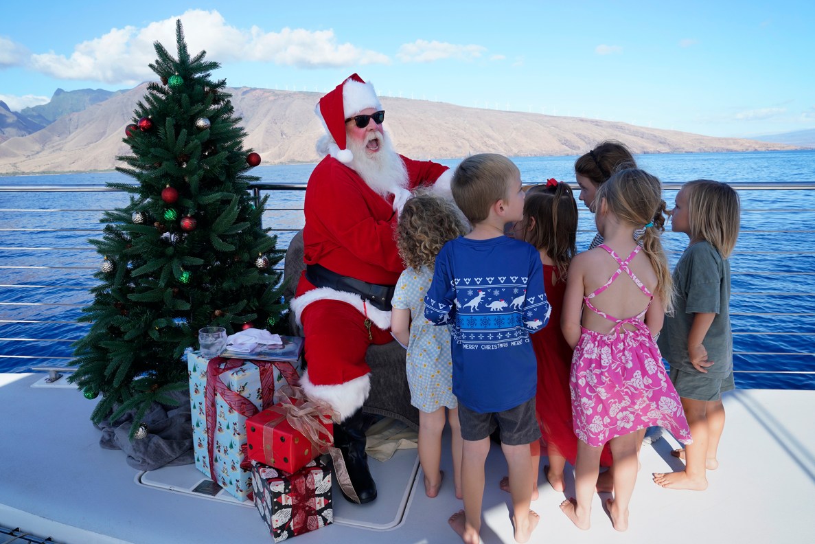 Ron Proctor reads a book to the keiki on the Alii Nui Sunset Sail Santa Cruise Saturday, Nov. 25, 2023, in Maalaea Harbor in Wailuku. Proctor has played Santa for more than 25 years. He lost his Lahaina home and belongings, including the hand-made Santa suit his daughter made, in the Aug. 8 fire. (Kevin Fujii/Civil Beat/2023)
