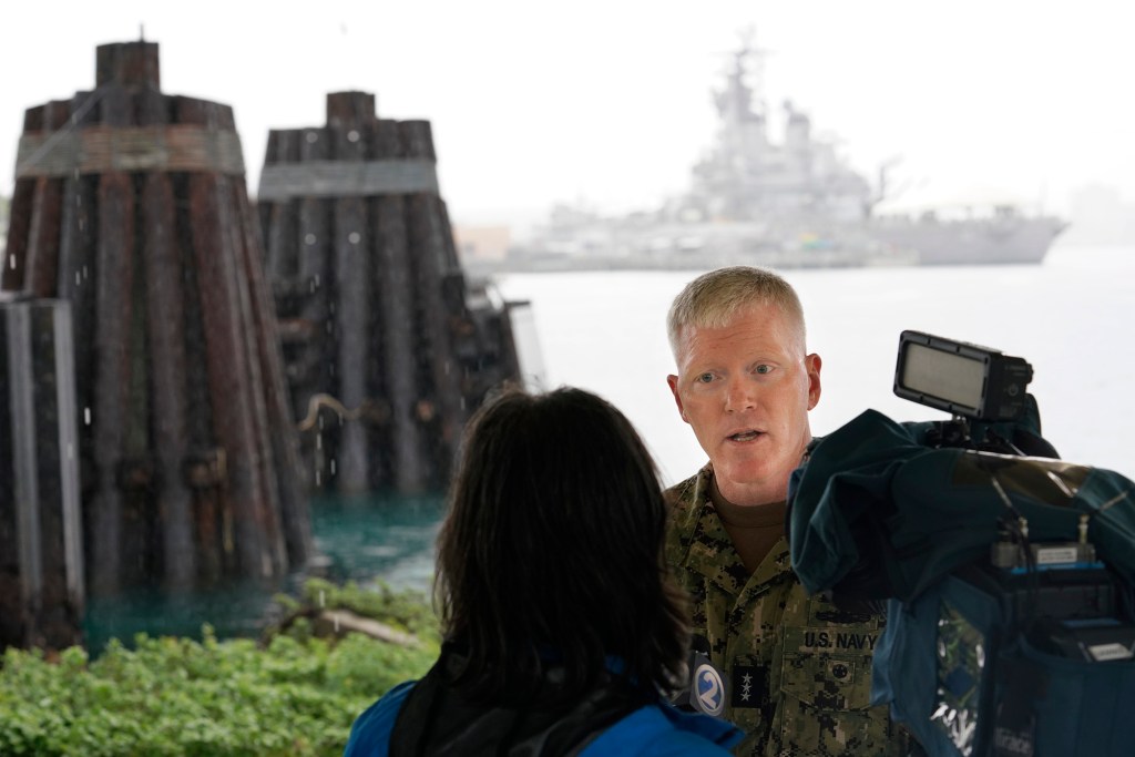 Joint Task Force - Red Hill vice-admiral John Wade, from left, does a TV interview Wednesday, Dec. 20, 2023, at Joint Base Pearl Harbor-Hickam in Honolulu. The USS Missouri sits in the background. Today marks the completion of gravity based defueling of Red Hill Bulk Fuel Storage Facility. Defueling began Oct. 16 and removed approximately 104,642,160 gallons of fuel. Gravity based defueling has been completed six months ahead of schedule. (Kevin Fujii/Civil Beat/2023)