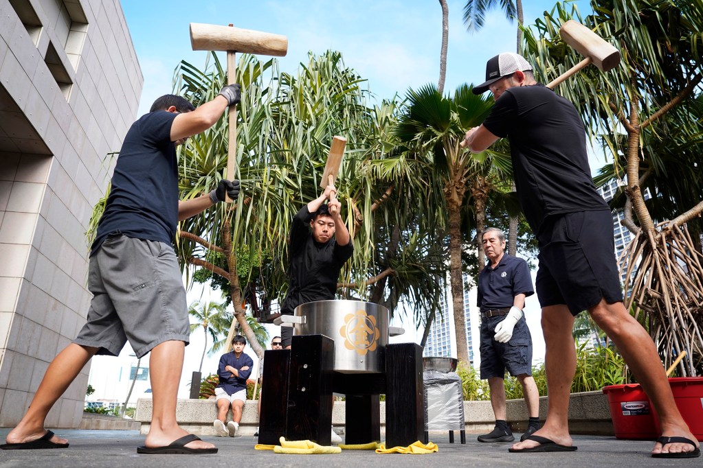 The Konko Mission of Wahiawa’s Clayton Matsuoka, from left, Bruce Adkison and David Yano use kine (wooden mallets) during a traditional new year’s mochitsuki (mochi pounding) demonstration for Prince Waikiki Hotel guests Wednesday, Dec. 27, 2023, in Honolulu. Head minister Rev. Yasuhiro Yano, second right, stands by to add just the right amount of water to make the mochi pliable and prevent sticking. The making of mochi (chewy rice cake) and consuming it is a Japanese new year tradition. Eating mochi is said to bring good luck. (Kevin Fujii/Civil Beat/2023)