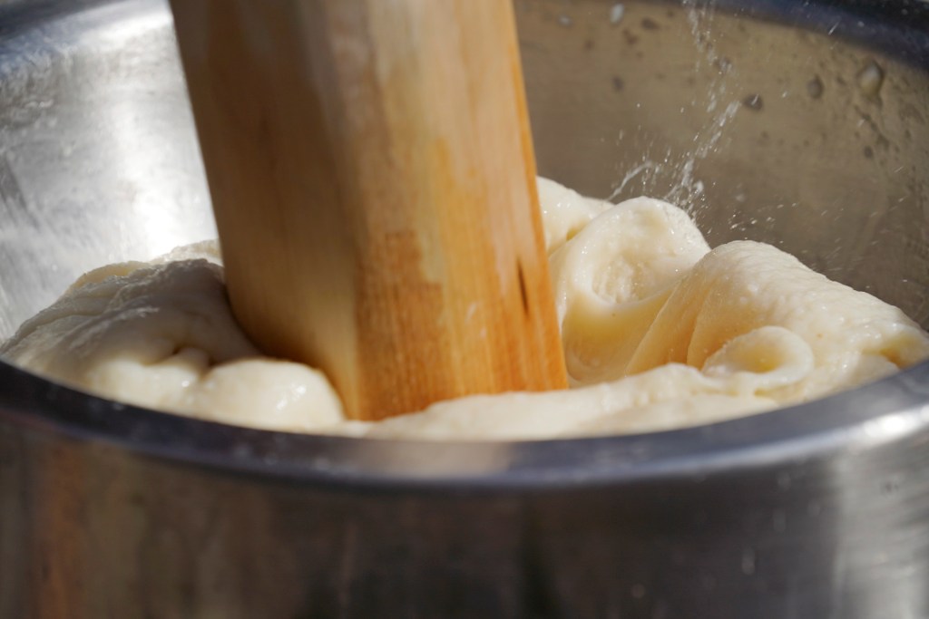 During the rhythm of mochitsuki (mochi pounding), a kine (wooden mallet) smashes mochi rice and alternates strikes with a hand to reset and fluff the mochi for the next strike as shown during a Konko Mission of Wahiawa’s mochitsuki demonstration for Prince Waikiki Hotel guests Wednesday, Dec. 27, 2023, in Honolulu. The making of mochi (chewy rice cake) and consuming it is a Japanese new year tradition. Eating mochi is said to bring good luck. (Kevin Fujii/Civil Beat/2023)